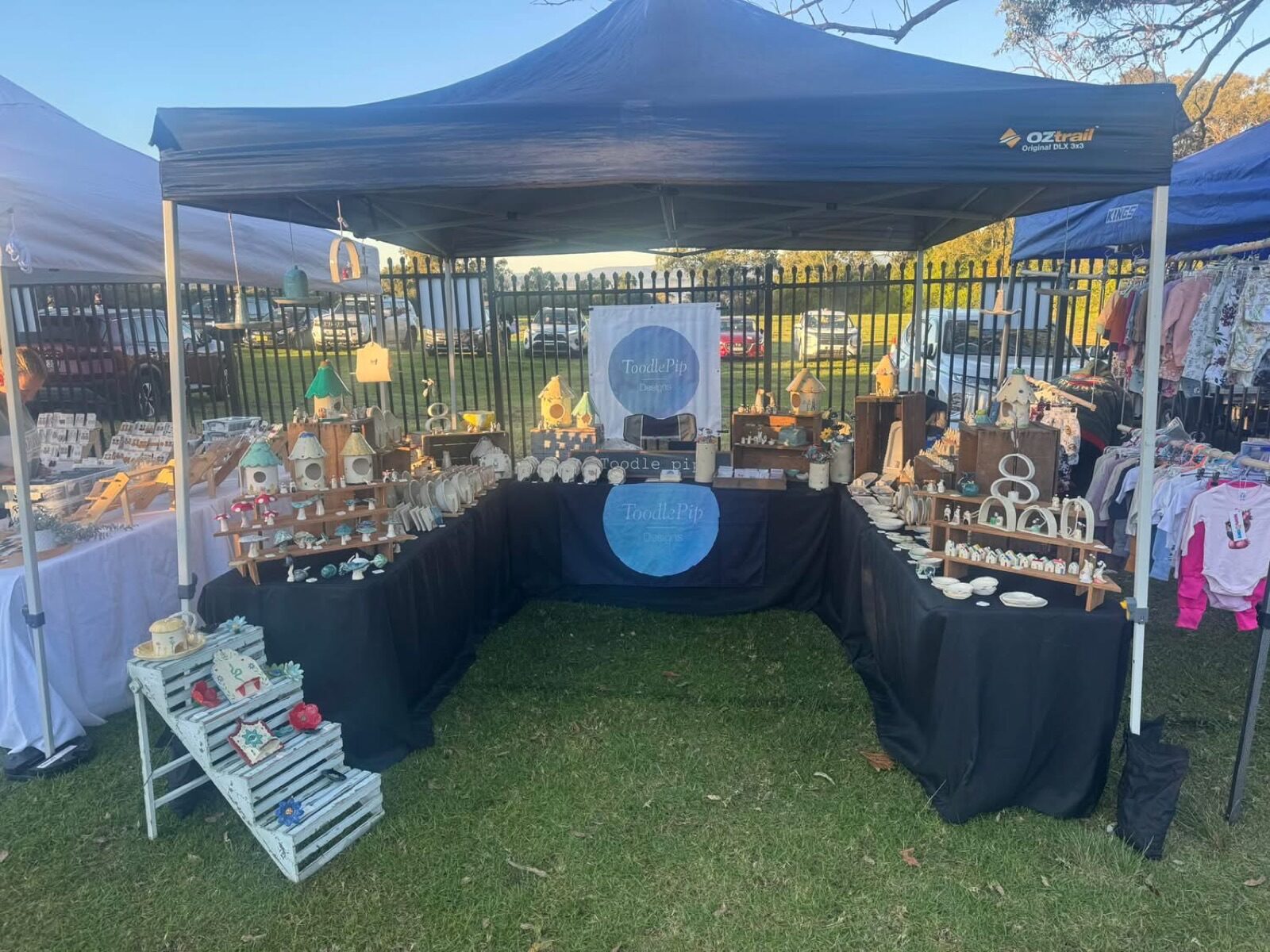 Toodle Pip Designs market stall at Cobbitty Village Markets, with hand-built ceramic houses and bird houses laid out on a black-draped table under a marquee.